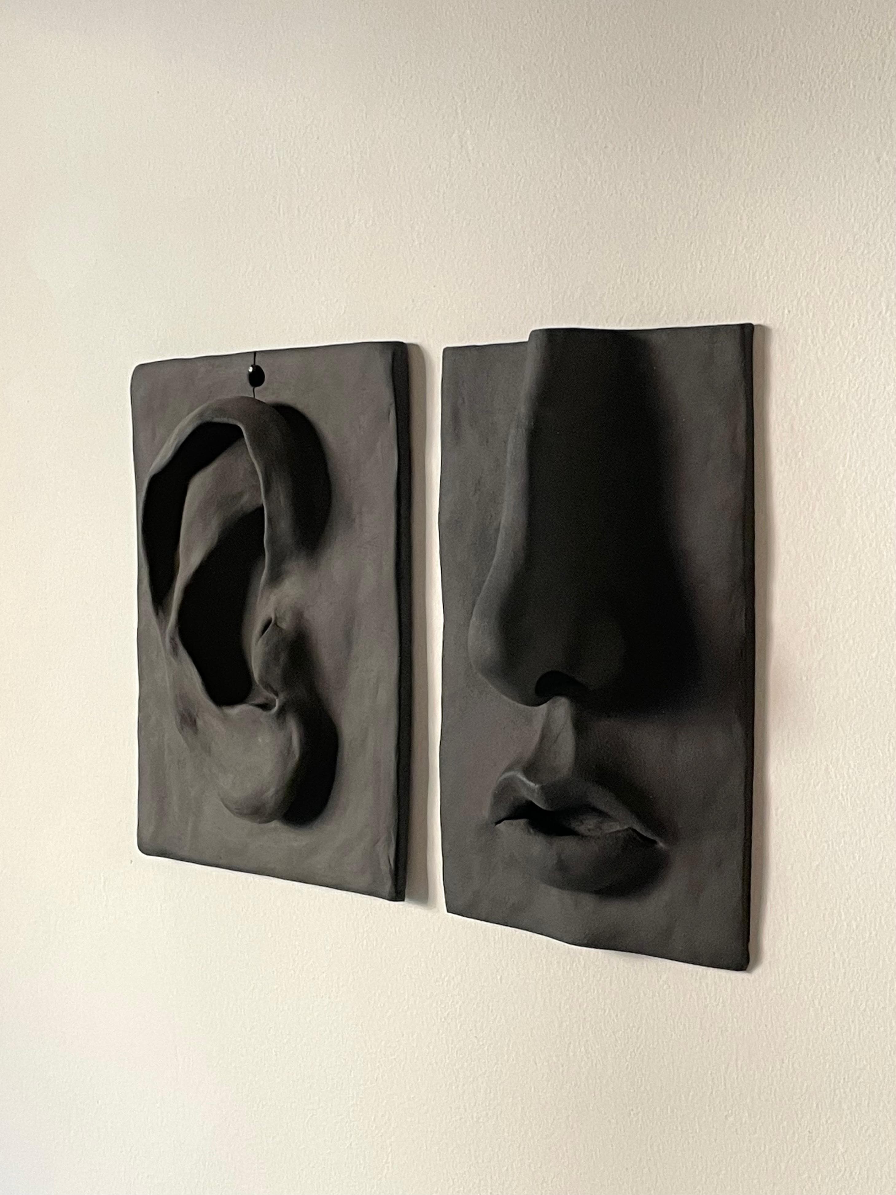 Wall sculptures of an ear and face in dark clay